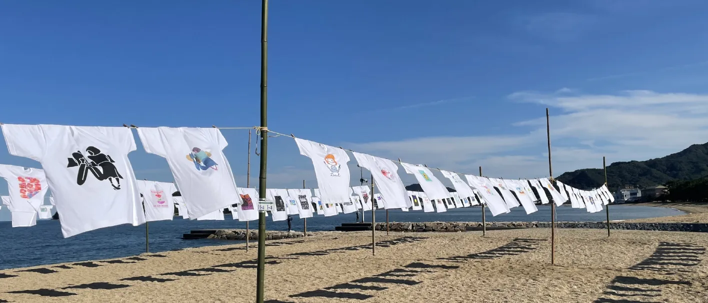 浜辺でたくさんの白Tシャツを干している様子
